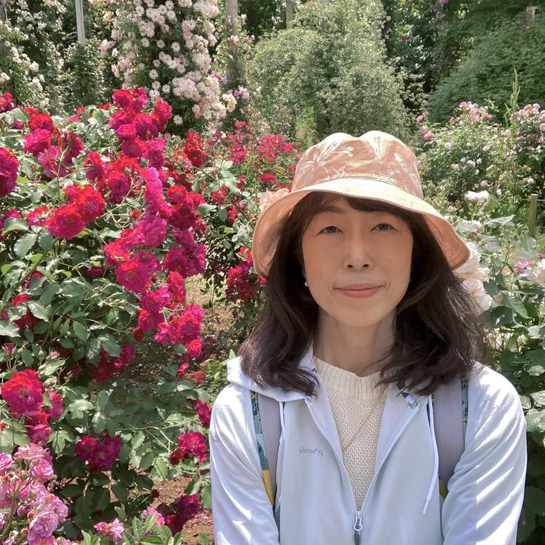 京成バラ園の色とりどりのバラを背景にした小畑真由美さん、2023年